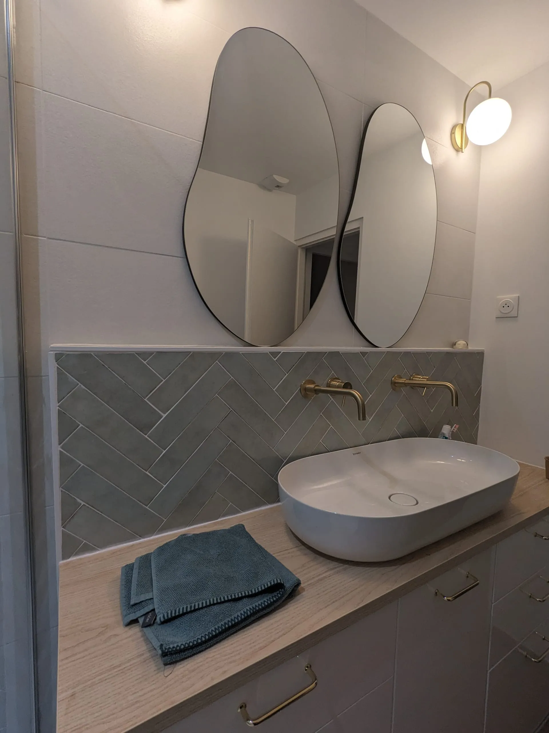 Meuble double vasque en bois avec miroirs ovales, robinets en laiton et crédence en chevrons