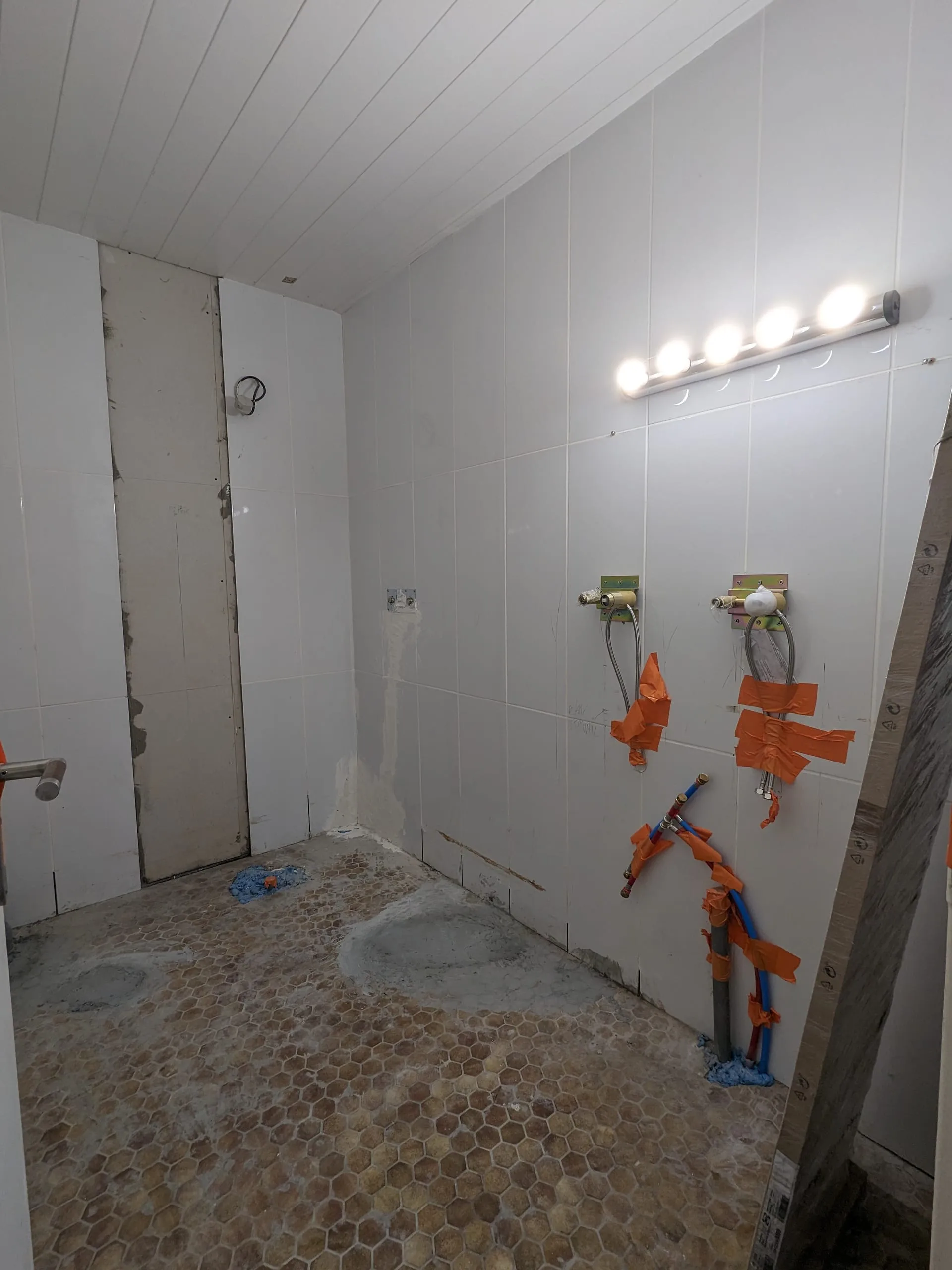Salle de bain en cours de chantier avec arrivées d’eau apparentes, carrelage mural et sol en mosaïque