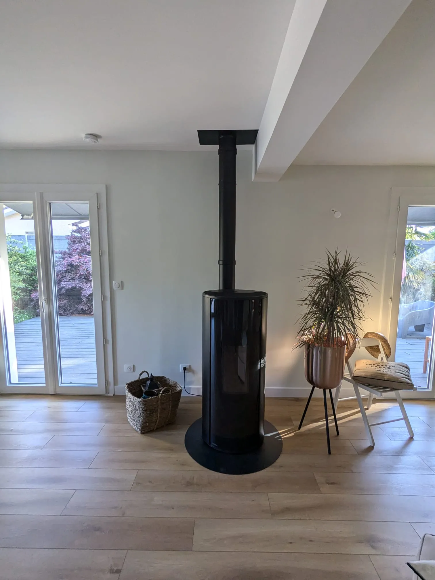 Poêle noir central dans une pièce claire avec sol bois et portes-fenêtres donnant sur la terrasse