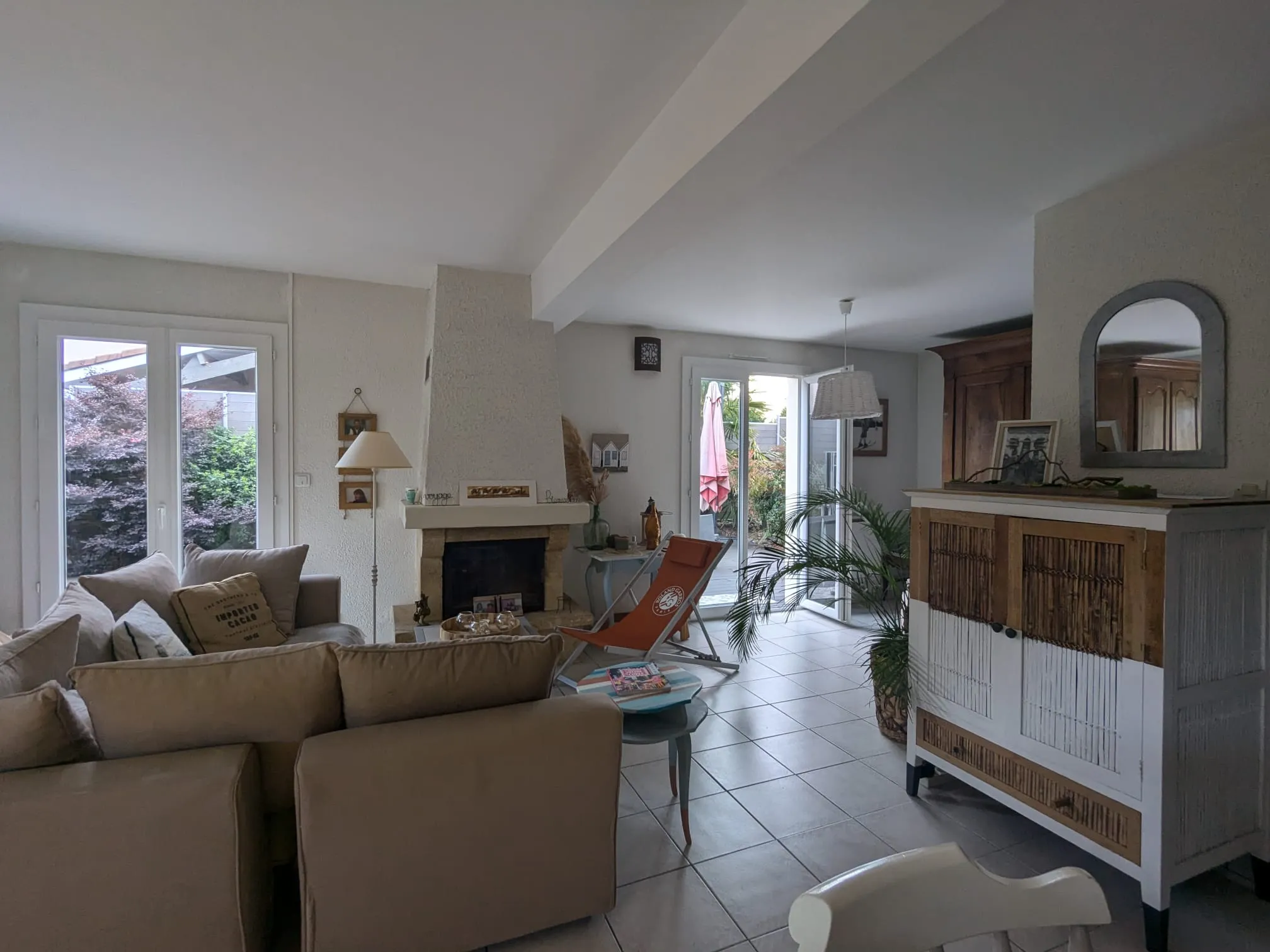 Séjour familial avant travaux avec canapé beige, cheminée, meuble bas et portes donnant sur la terrasse
