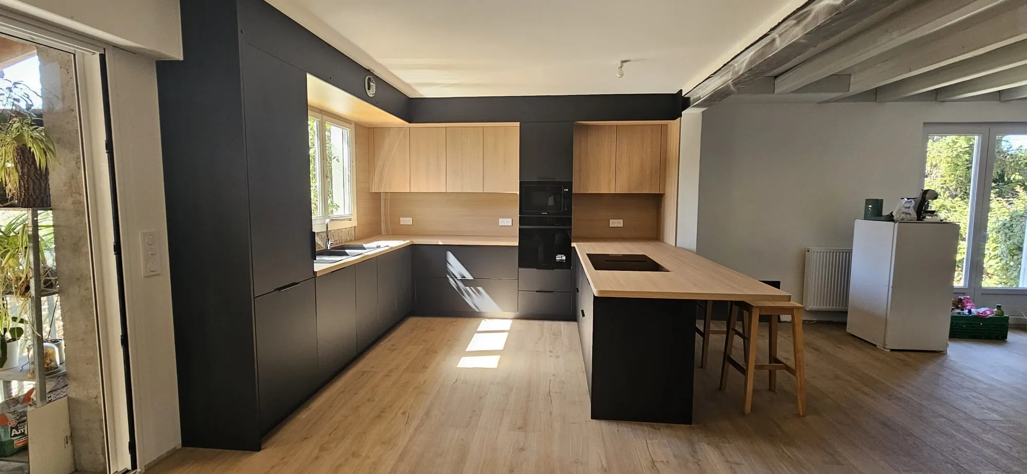 Cuisine terminée avec façades noires, meubles hauts en bois clair et grand plan de travail