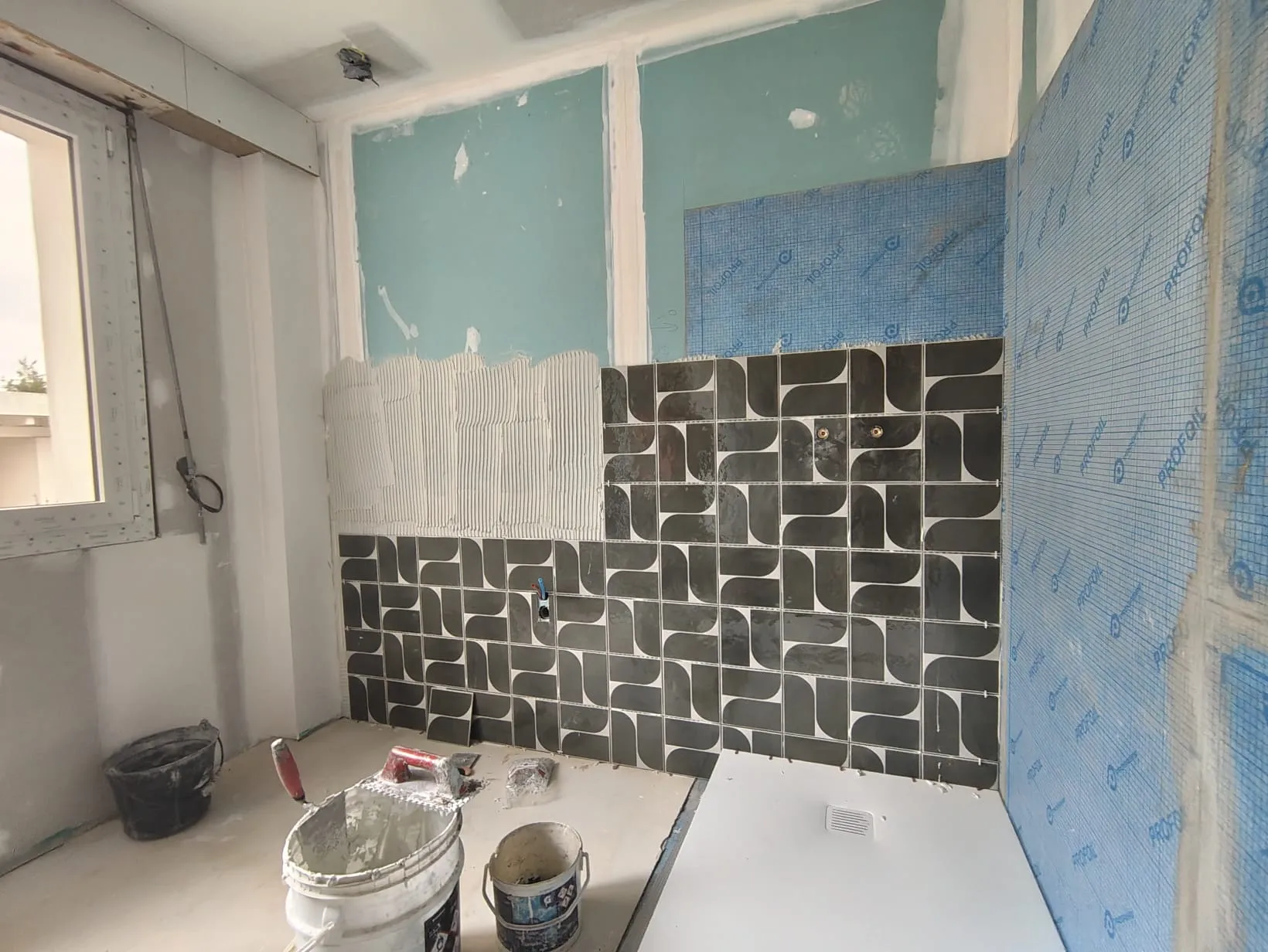 Douche en cours de pose avec carrelage géométrique noir et blanc et étanchéité murale