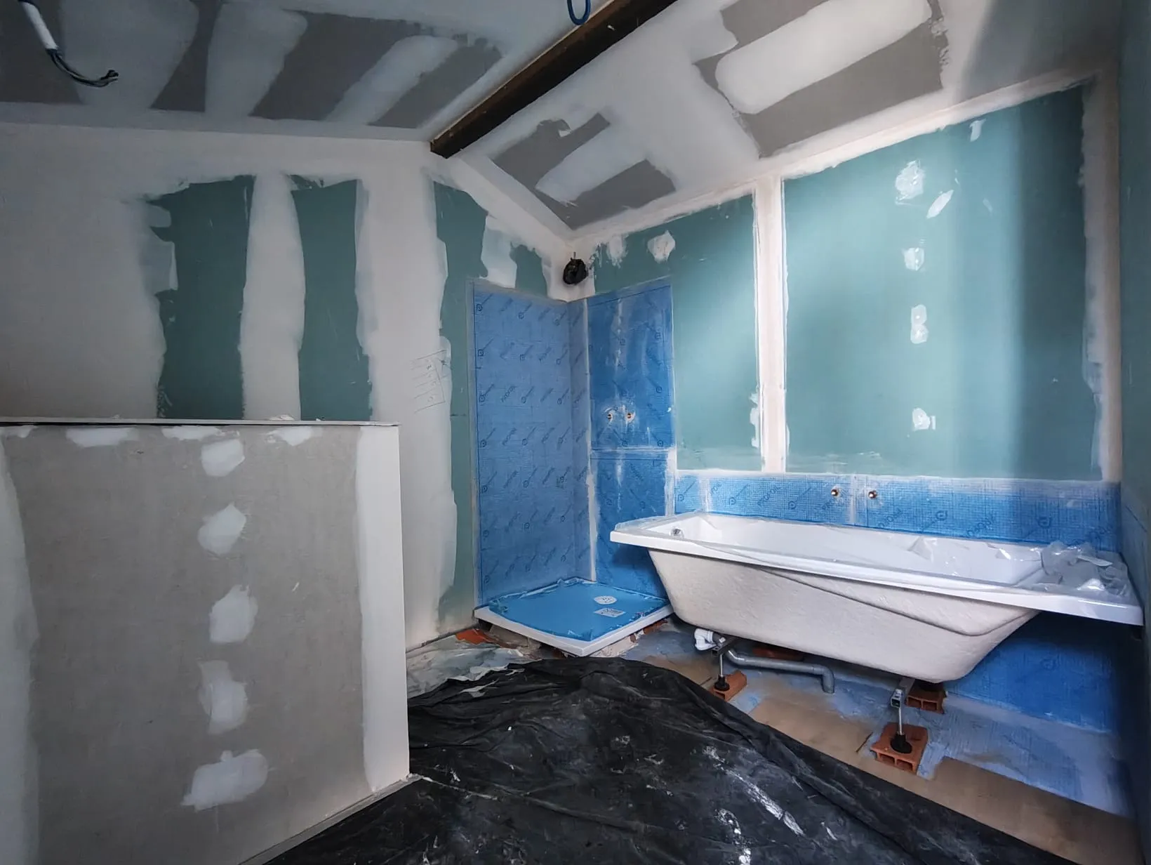 Salle de bain en cours de chantier avec baignoire, parois hydrofuges et douche en préparation