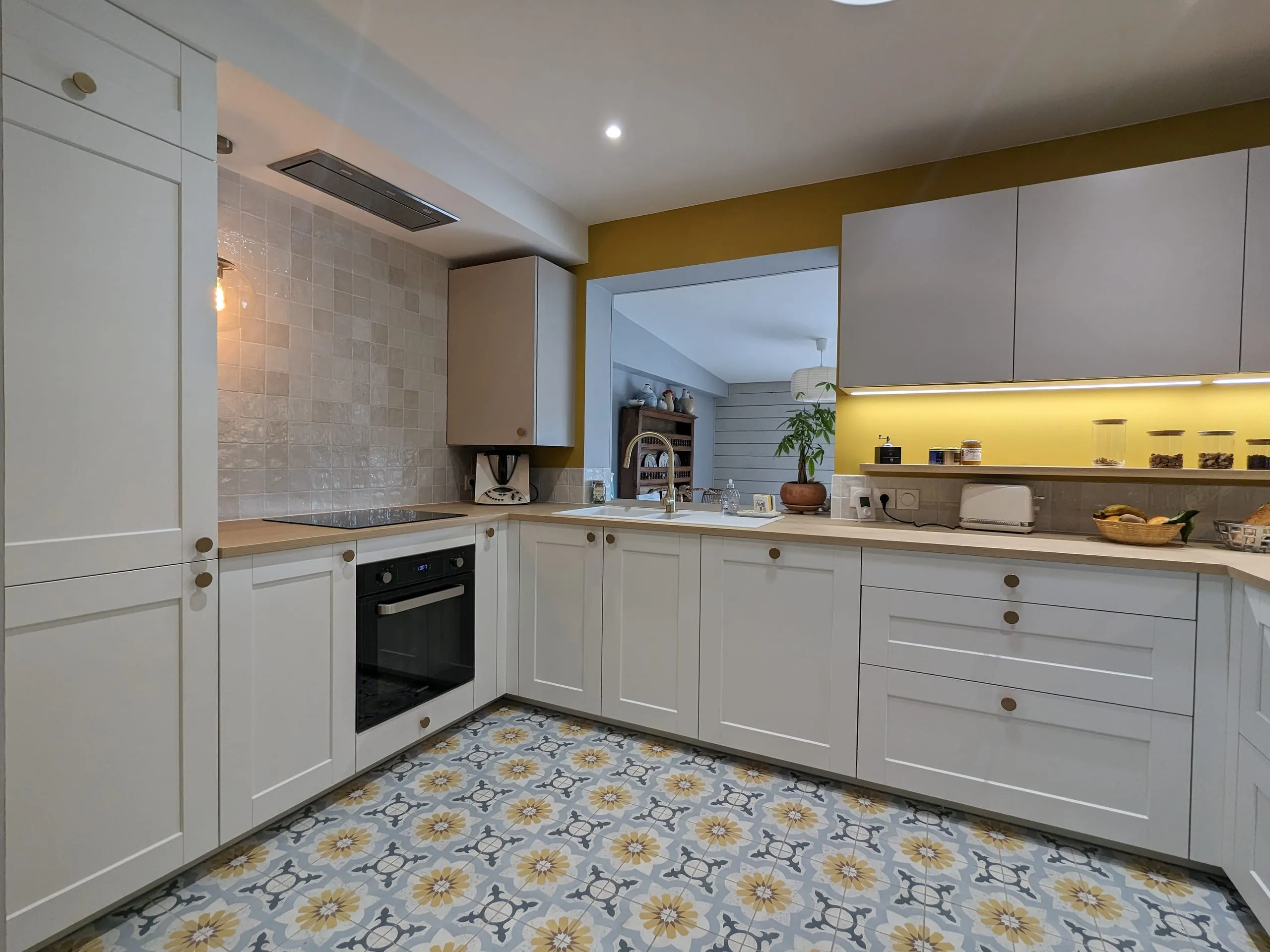 Cuisine blanche terminée avec mur moutarde, plan de travail en bois et sol à motifs