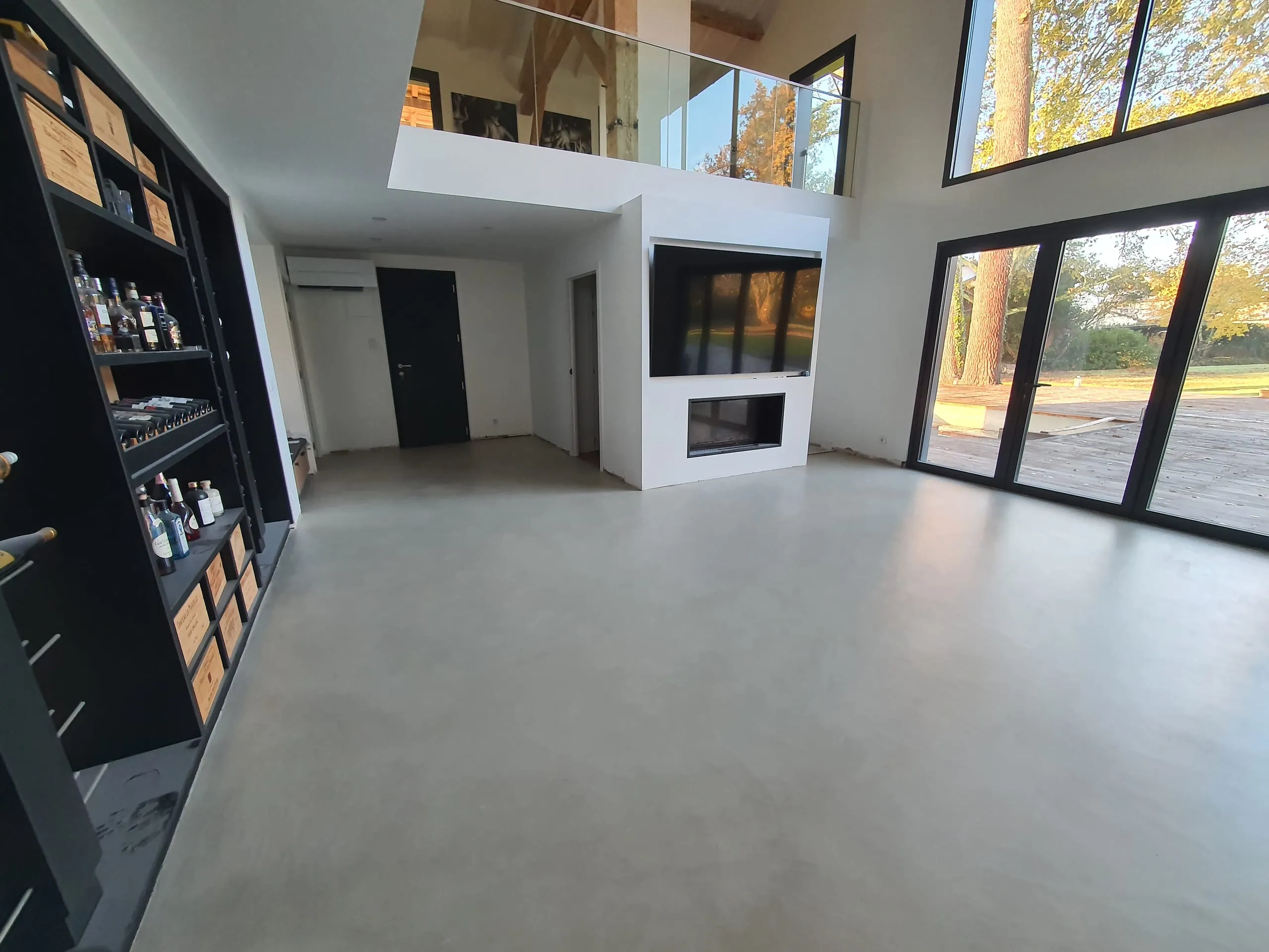 Pièce de vie lumineuse avec mezzanine vitrée, cheminée, grandes baies noires et meuble cave à vin